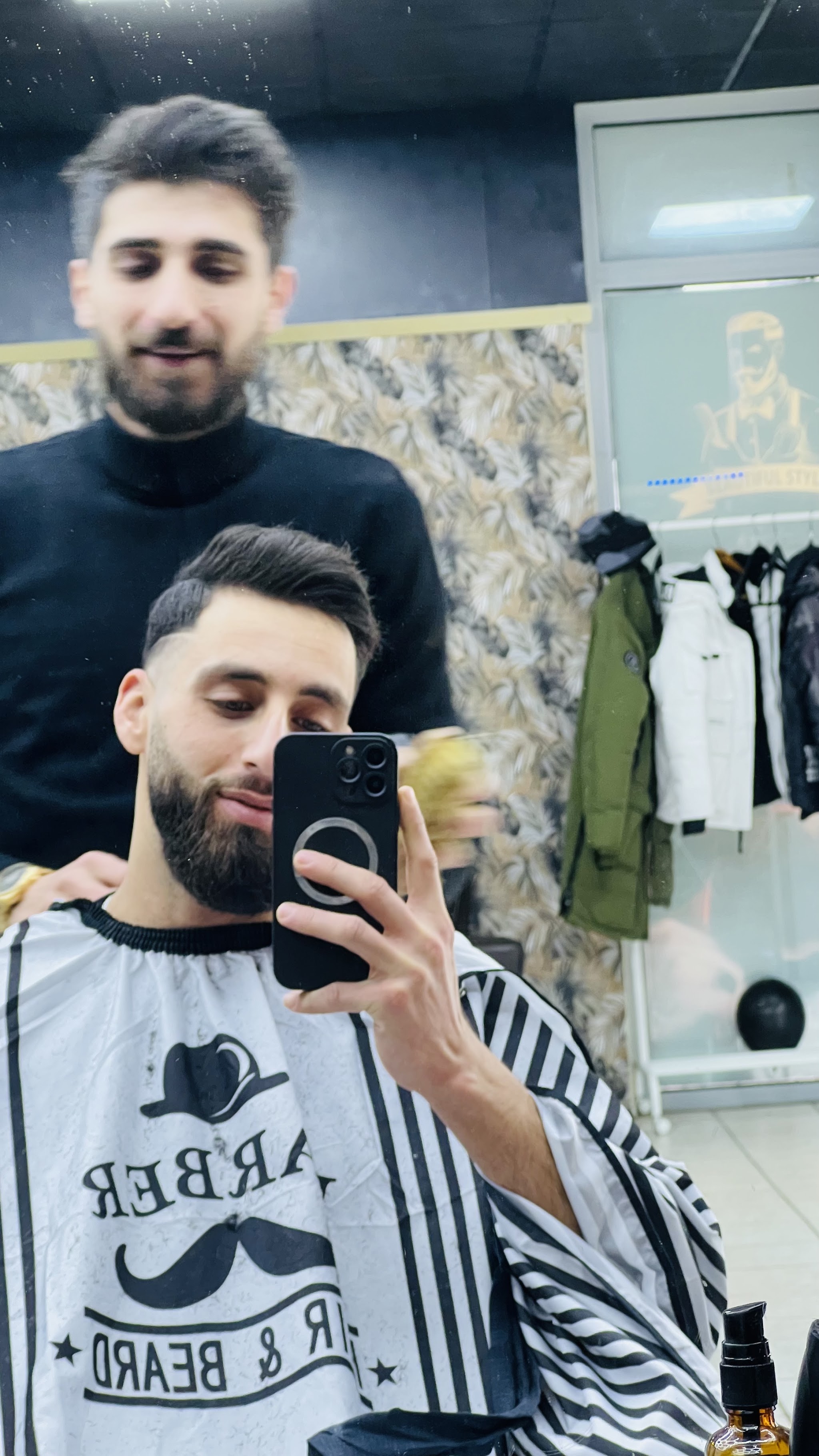 Klant in de stoel maakt een spiegelselfie, met de kapper achter hem